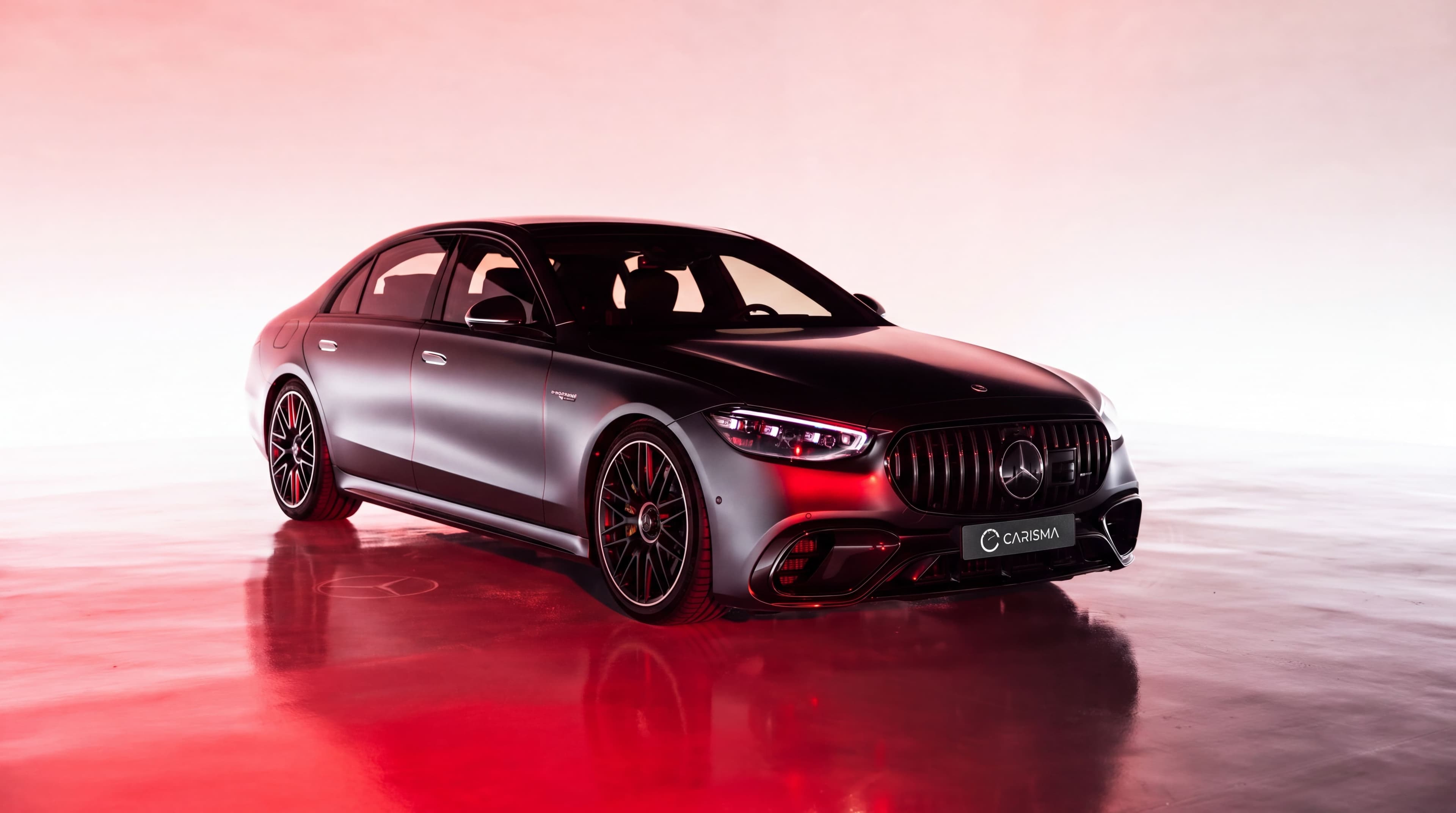 Berline Mercedes-AMG en studio sur un sol rouge réfléchissant, avec une plaque Carisma